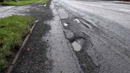 Pothole-damaged road surface with multiple cracks and broken tarmac along the edge of the carriageway in North Lincolnshire.