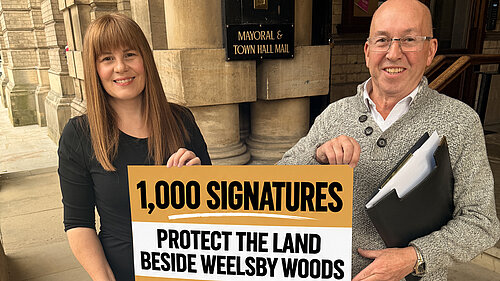 Cllr Nicola Aisthorpe and Liberal Democrat campaigner Brian Barrett holding a sign outside Grimsby Town Hall celebrating 1,000 petition signatures to protect land beside Weelsby Woods.